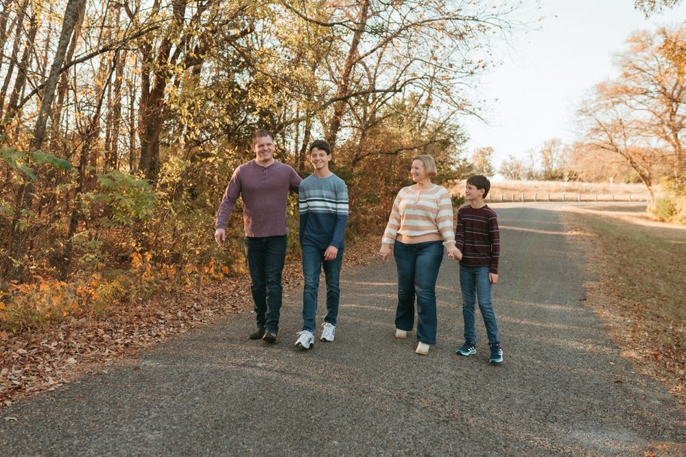 Family walking together on a tree-lined autumn path during golden hour sunset.