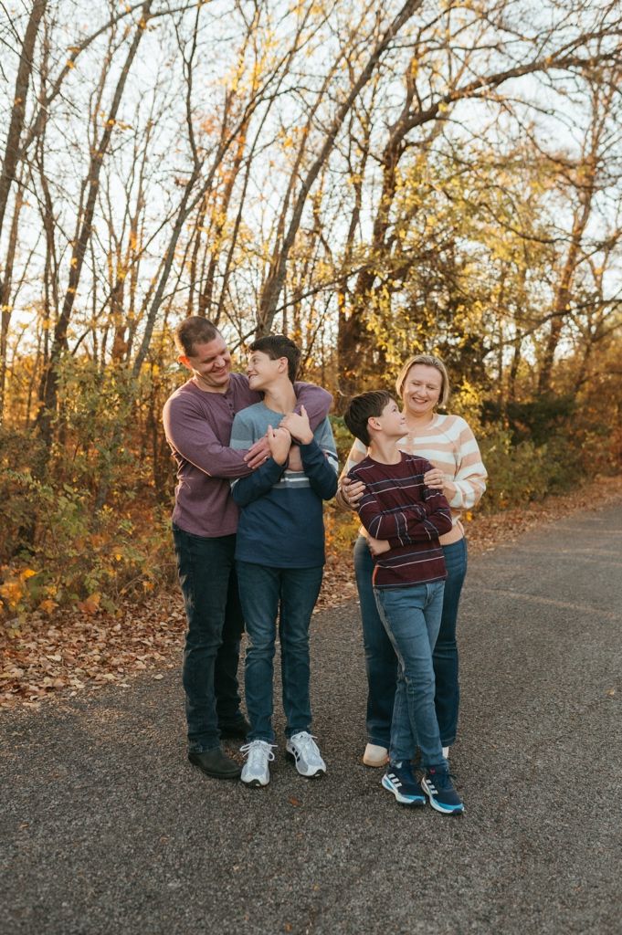 People embrace and share a joyful moment on a paved path surrounded by fall foliage.