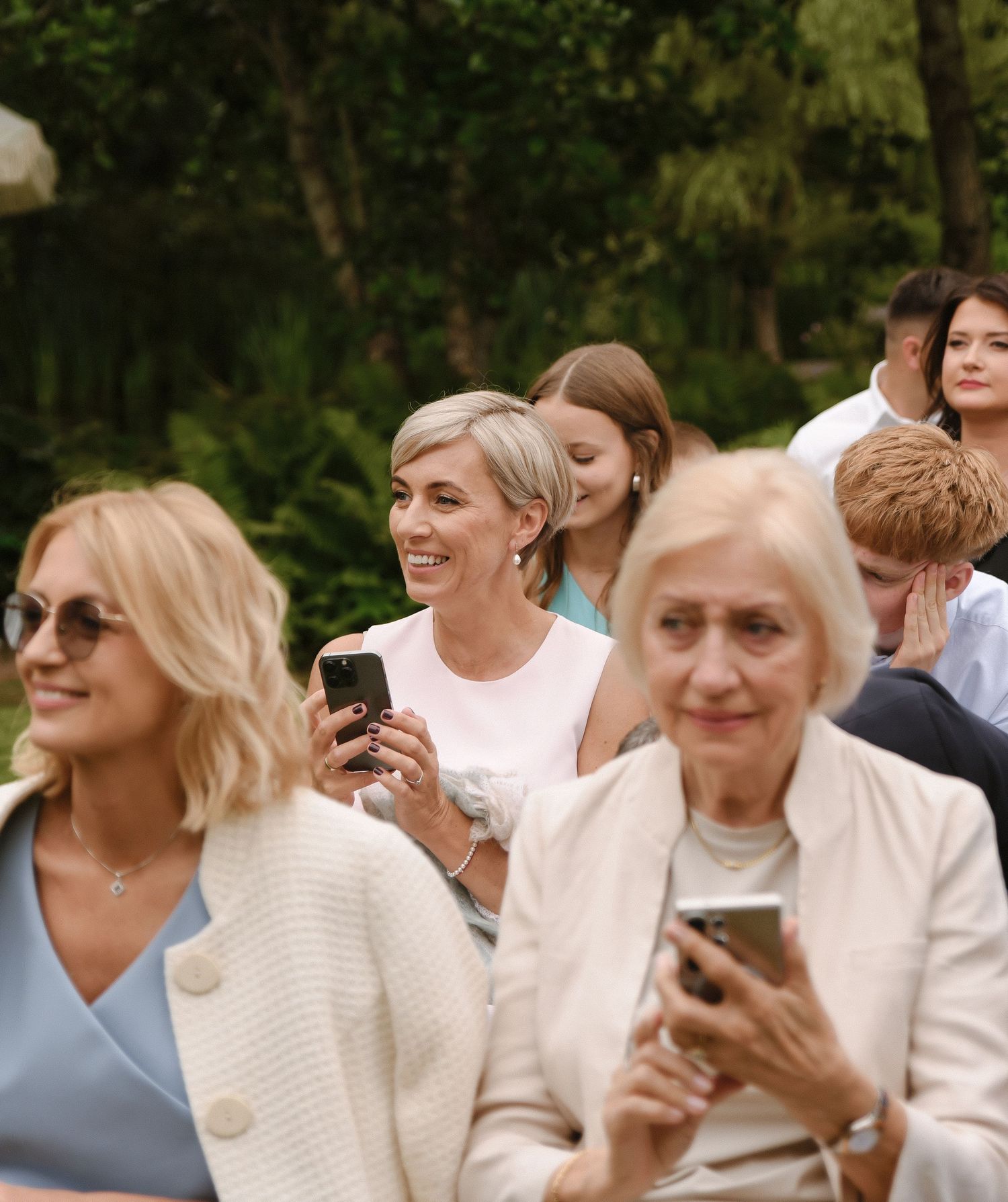 A group of people in white clothing smile and laugh together at an outdoor gathering.