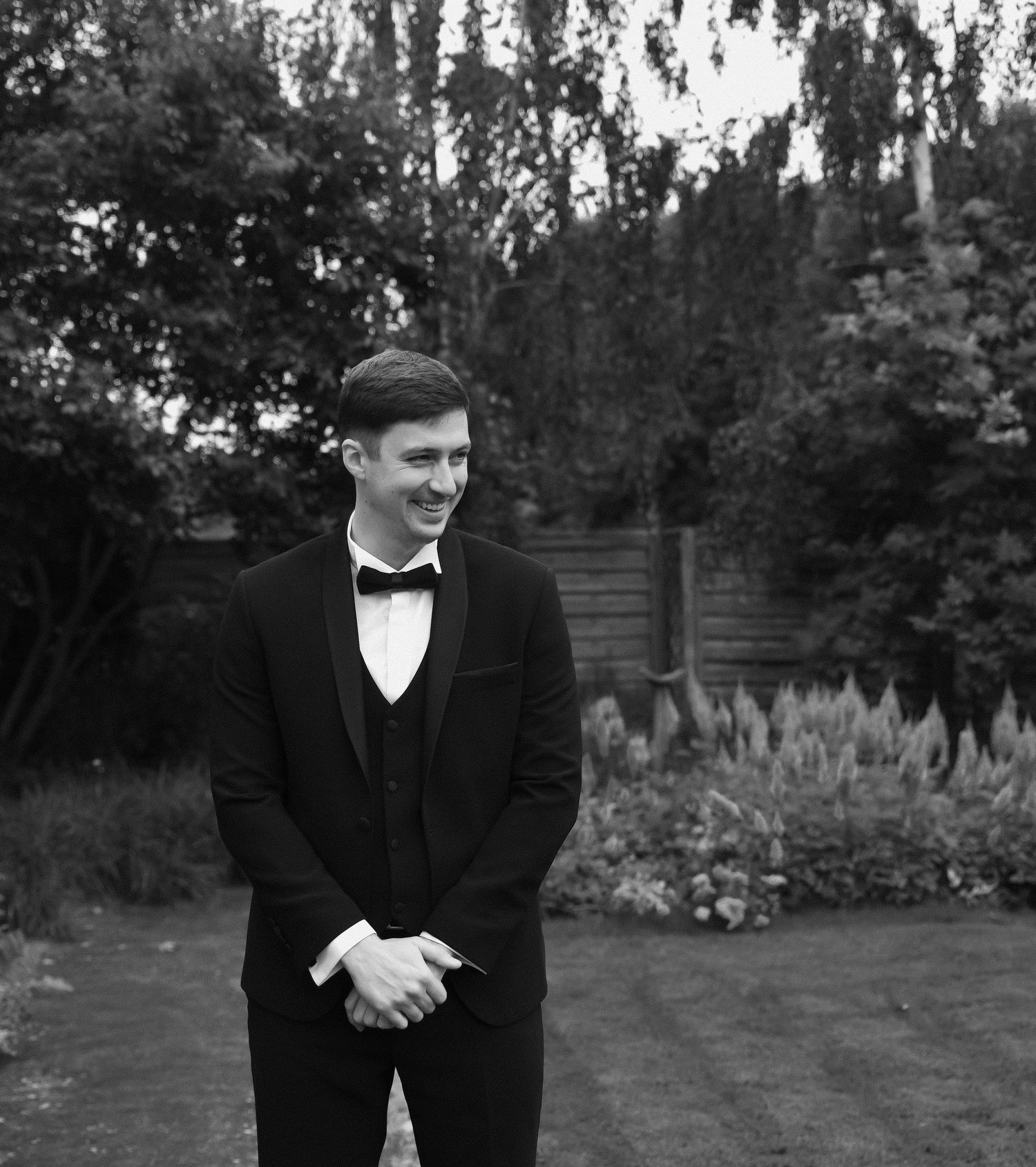 Black and white portrait series of someone in formal attire posing in a garden setting with trees and foliage.