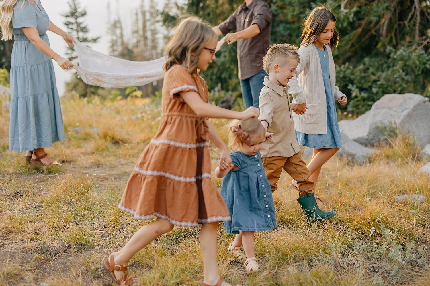 Children playing outdoors in a rustic field setting wearing vintage-style dresses and casual clothing.