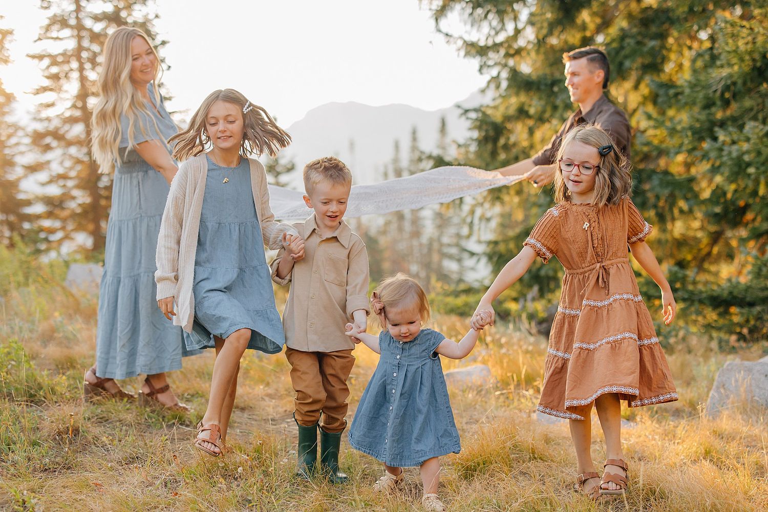 A family in coordinating brown and blue outfits poses together in a golden sunlit field during autumn.