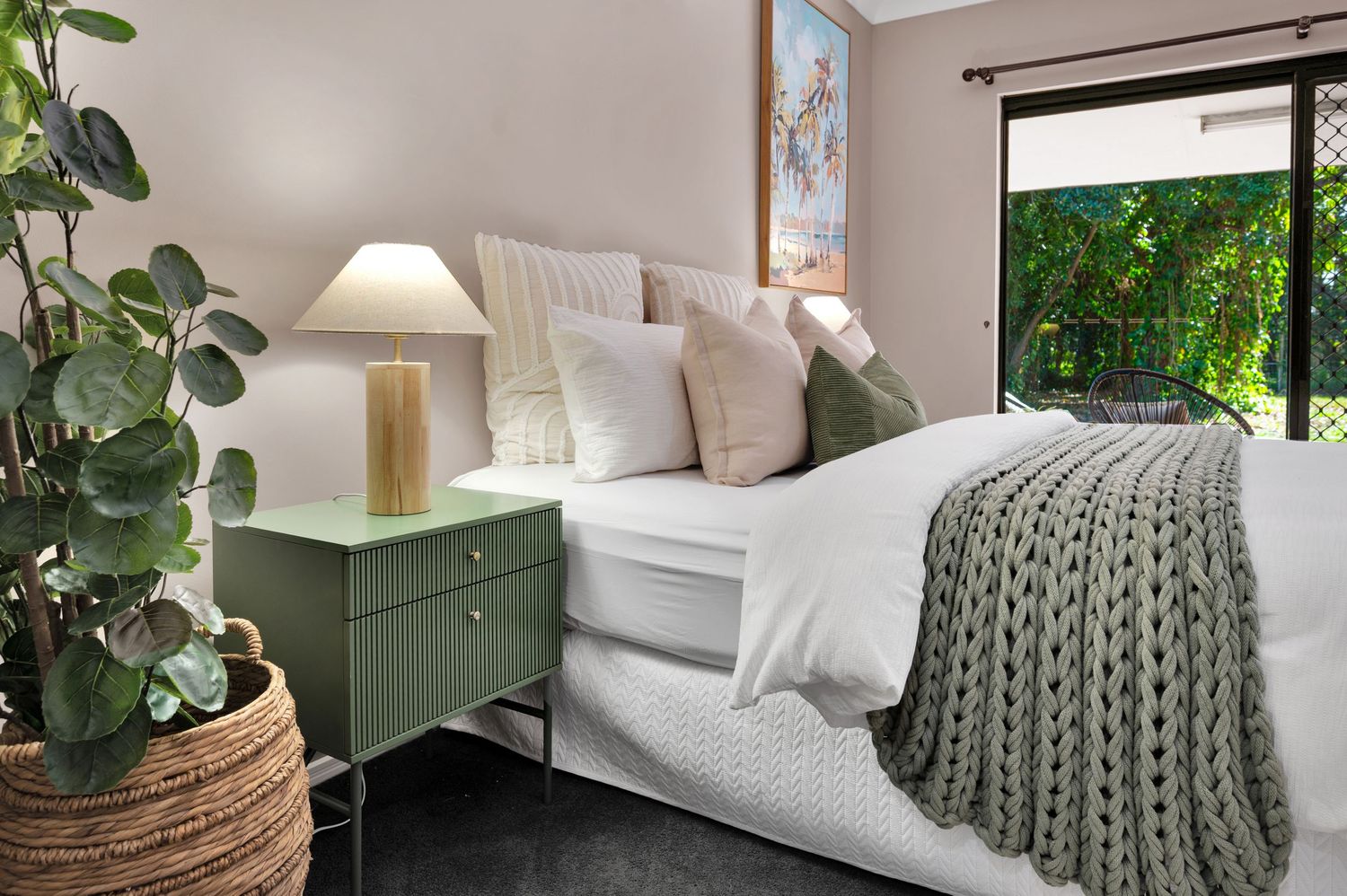 Cozy bedroom with white bedding, green accents, knitted throw blanket, and eucalyptus plants in natural decor.