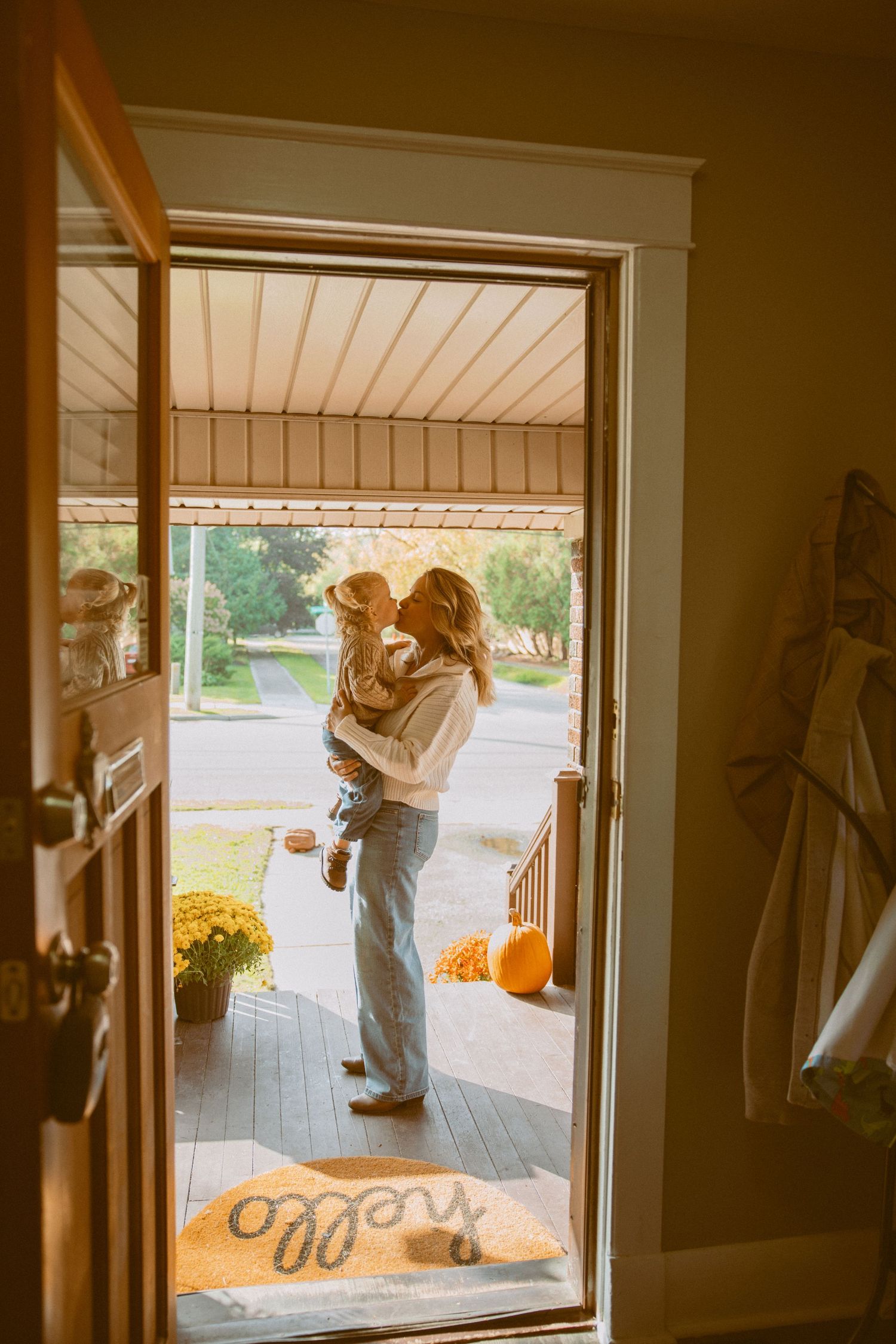 A couple embraces on a sunlit porch with autumn pumpkins and yellow flowers visible in the warm afternoon light.