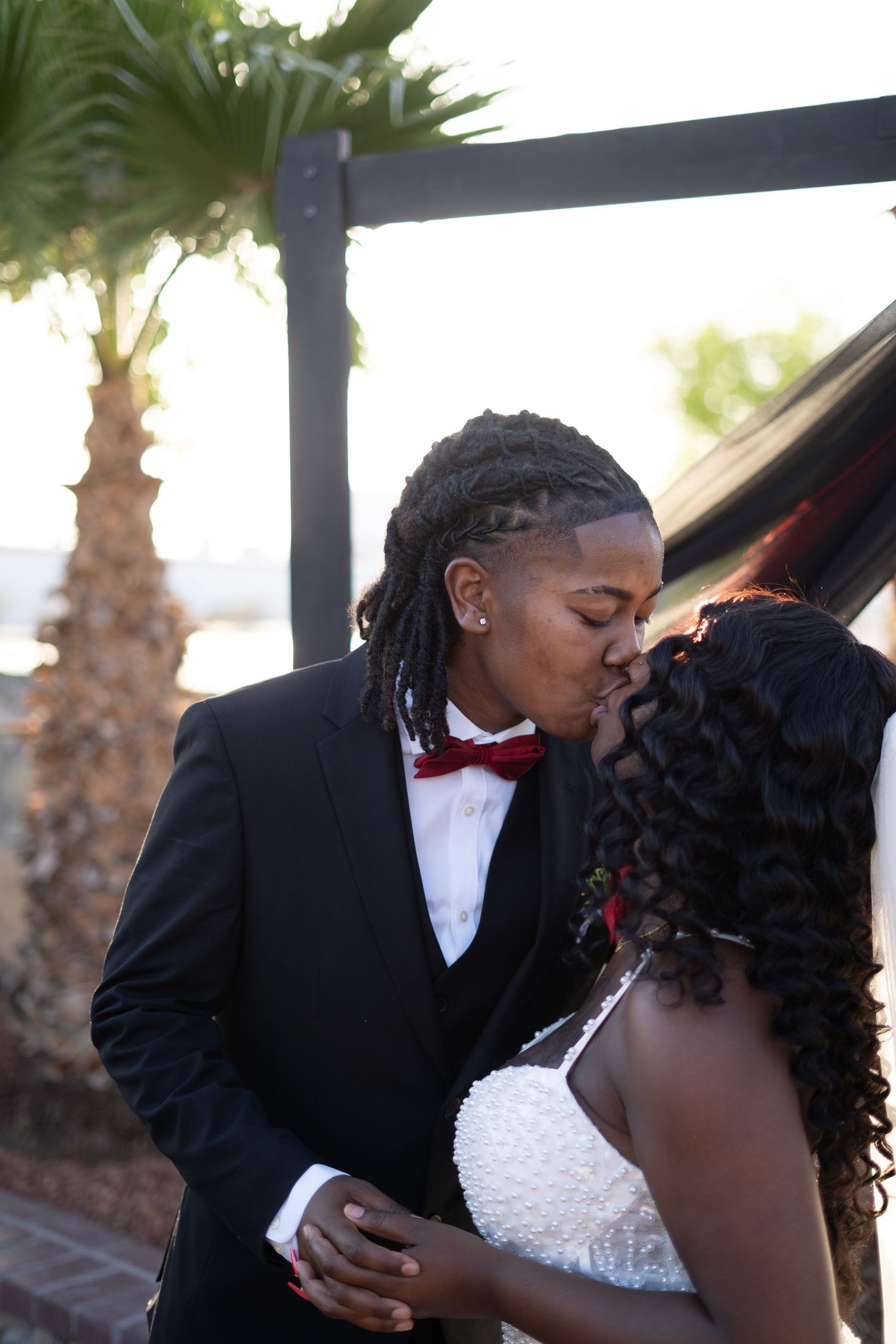 A romantic wedding couple shares a tender kiss under a palm tree-lined outdoor venue.
