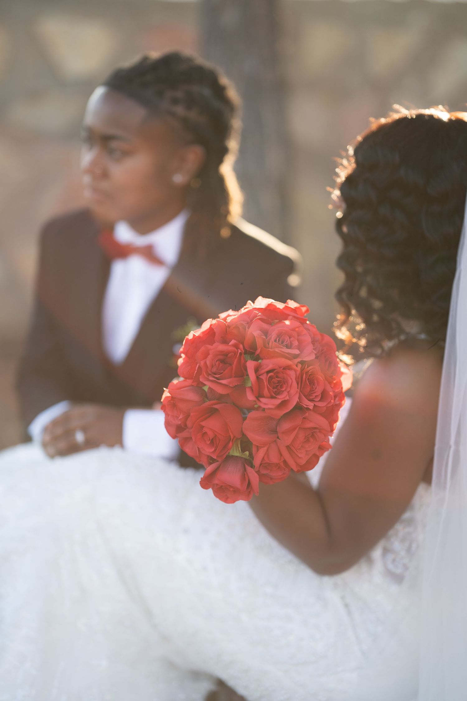 Artistic wedding portrait showing bright red rose bouquet against white bridal gown in soft focus.