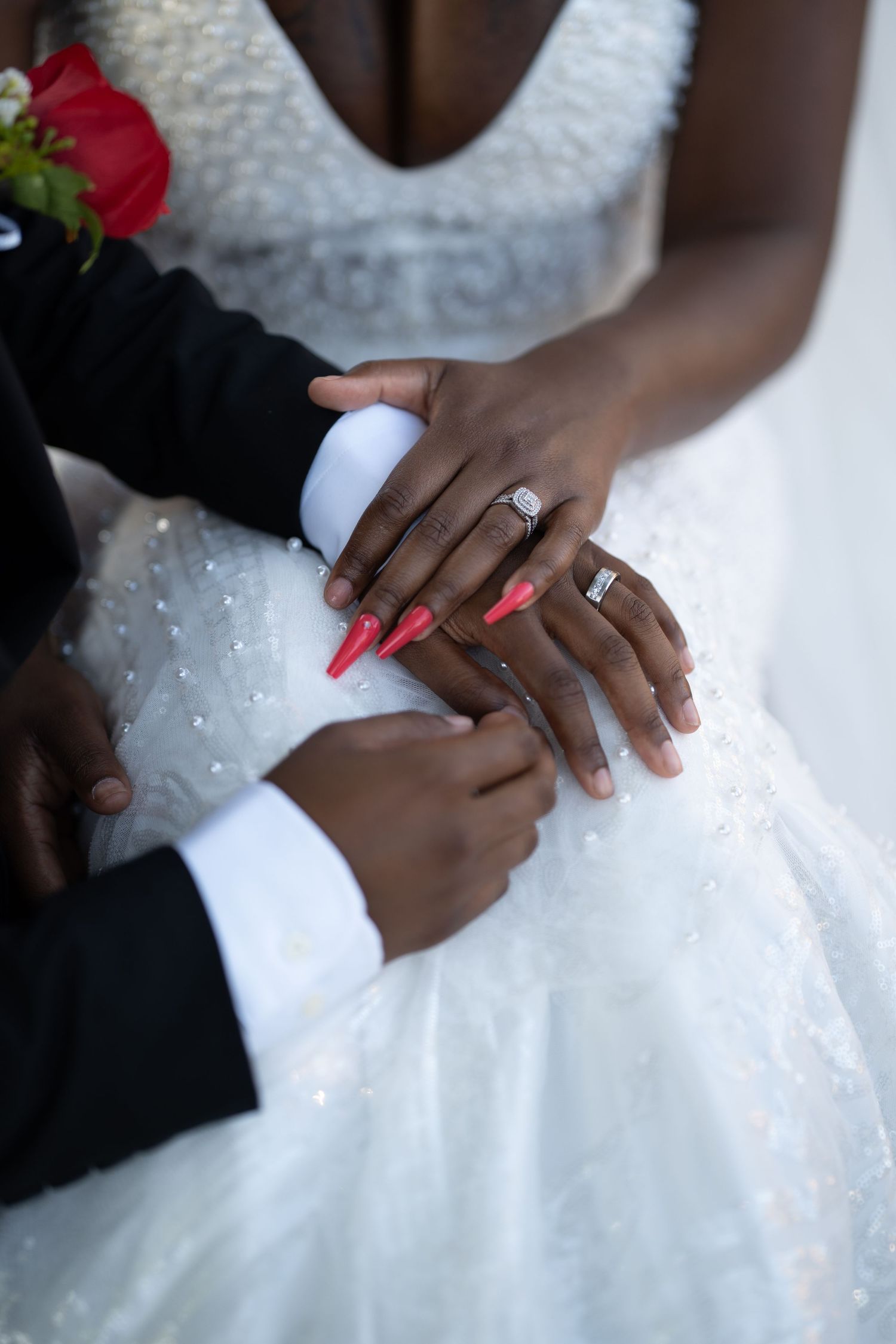 Close-up shots of hands wearing wedding rings with a white beaded wedding dress in the background.
