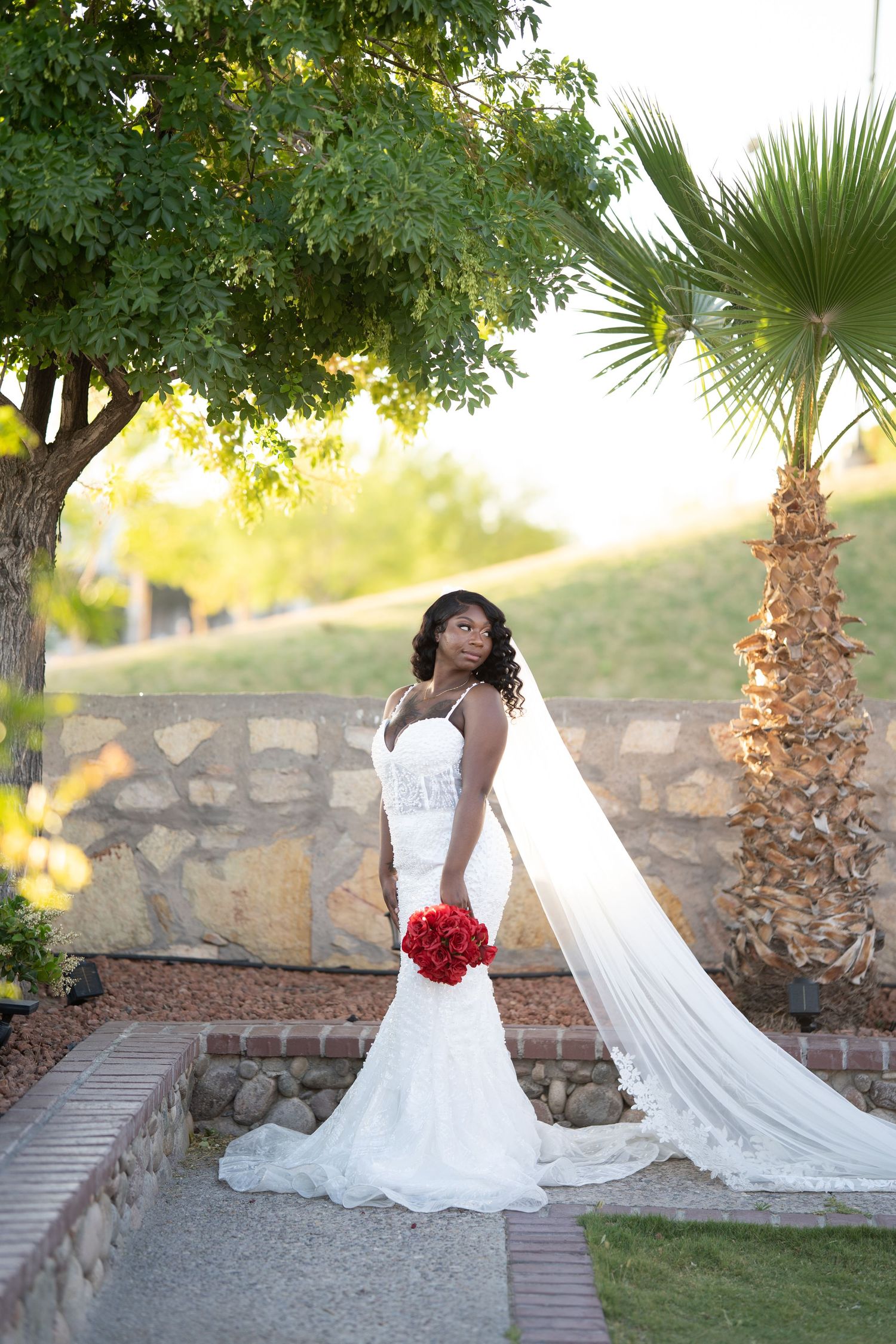 A stunning bridal portrait series showing a flowing white wedding gown and red bouquet against a garden backdrop.