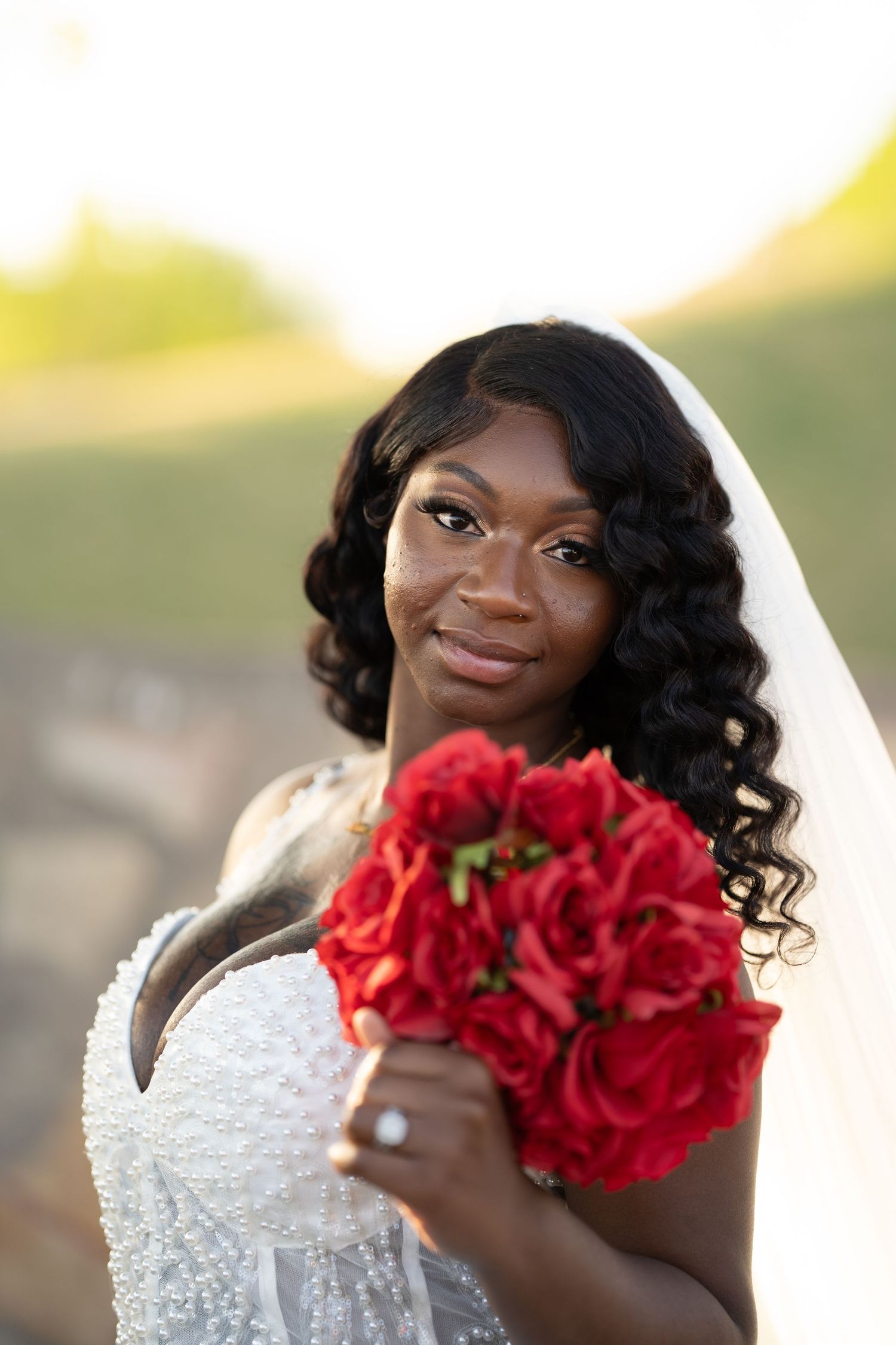 Close-up bridal portraits featuring a white beaded gown and vibrant red rose bouquet in golden sunlight.
