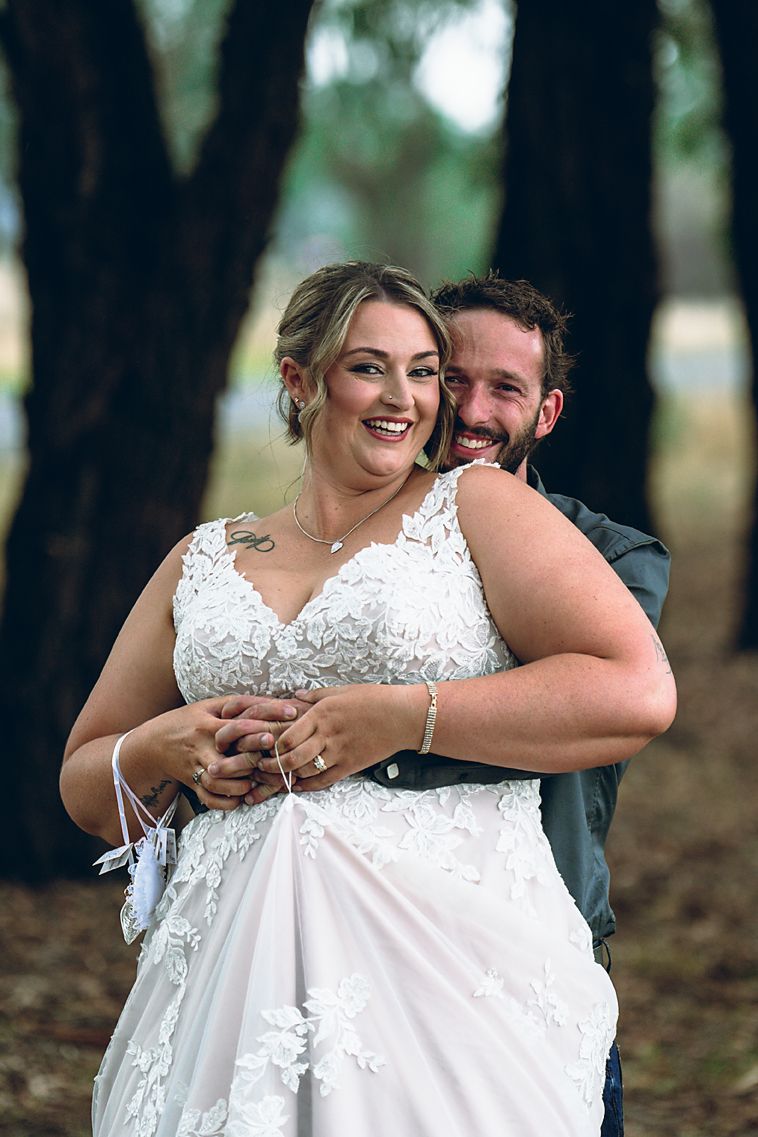 Happy newlywed couple embraces and laughs together in a wooded outdoor setting.