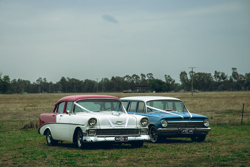 Classic vintage cars lined up in a grassy field with trees visible in the background.