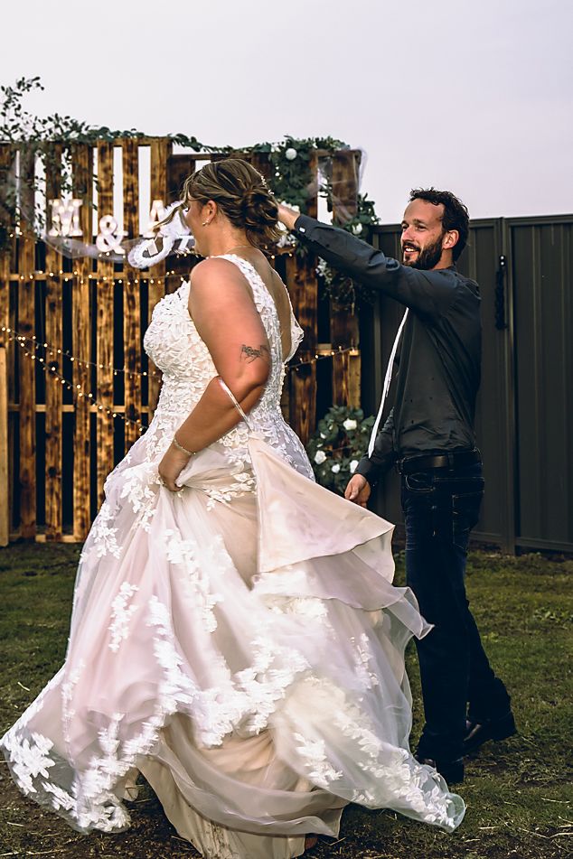 A couple in wedding attire dances together in a backyard, with the bride's white dress flowing gracefully in the motion.