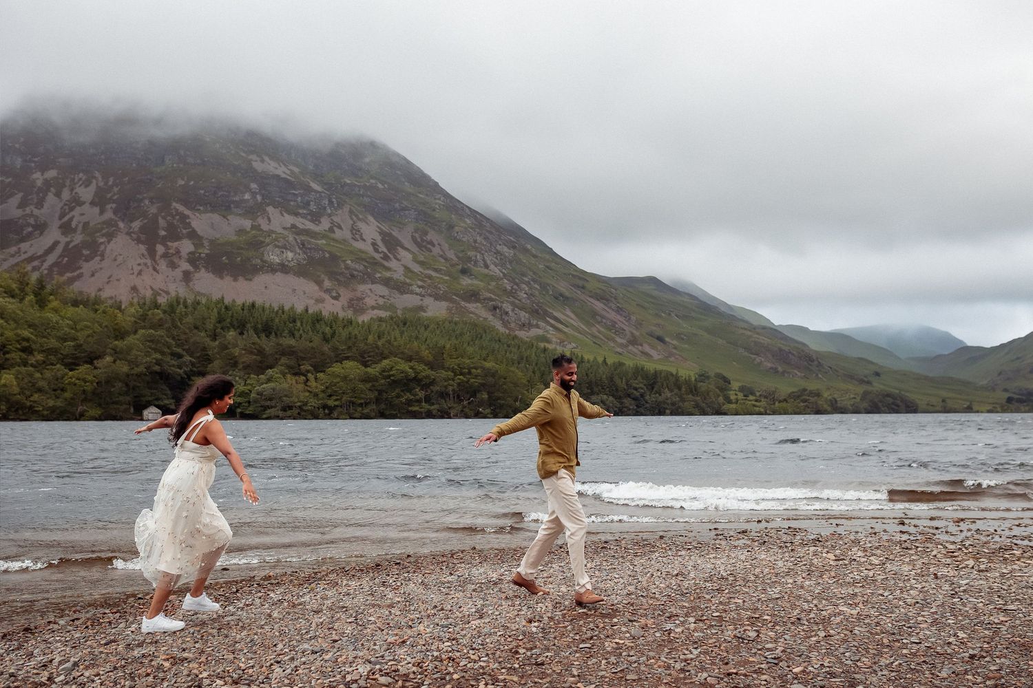 Lake District Engagement shoot.Two people share a joyful moment while walking along a gravel path in the Scottish Highlands on a winter day.