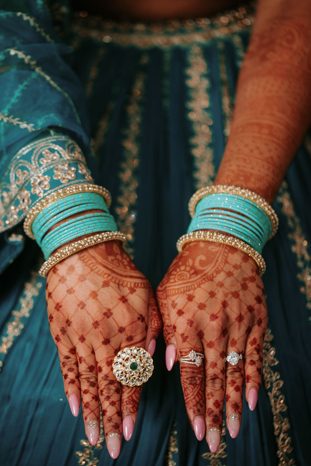 Hands adorned with intricate henna designs and turquoise bangles display elegant diamond rings and jewelry.