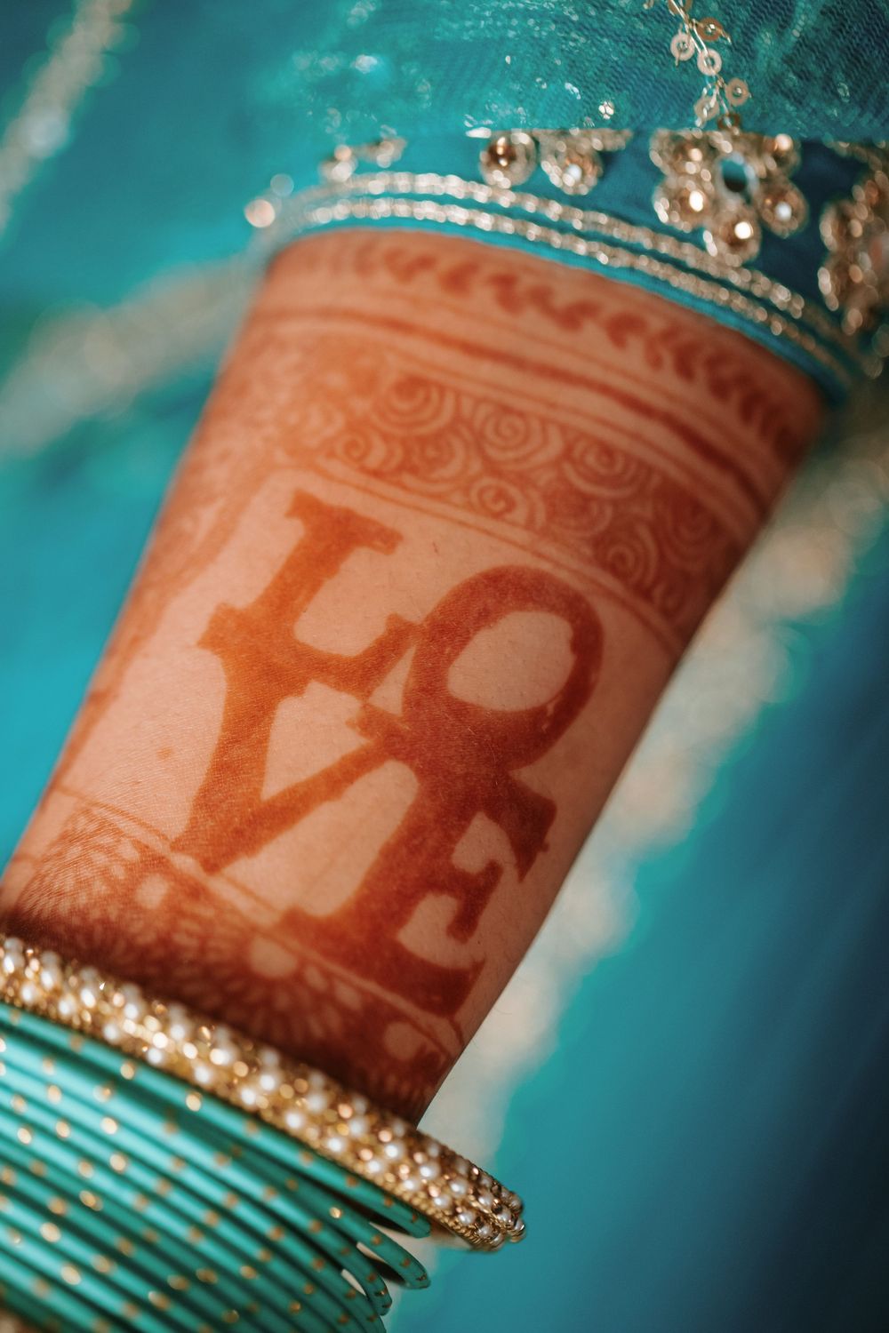 Close-up of mehndi art on arm with ornate bangles showing traditional Indian wedding details in turquoise setting.