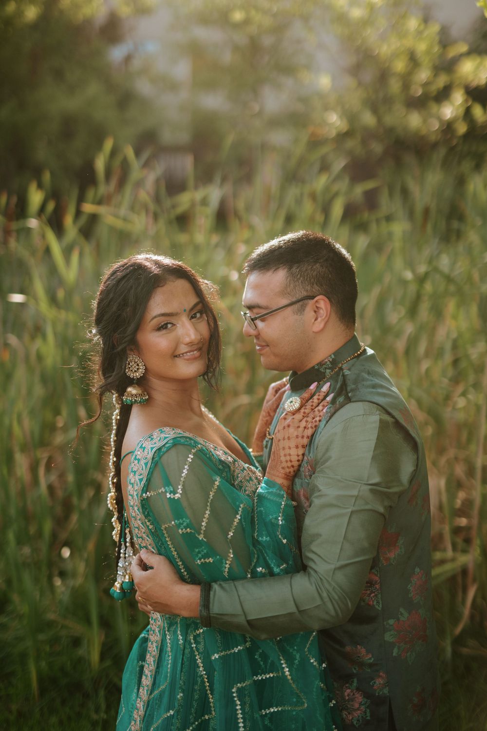 A romantic outdoor photoshoot in tall grass with a couple wearing green and casual attire at sunset.