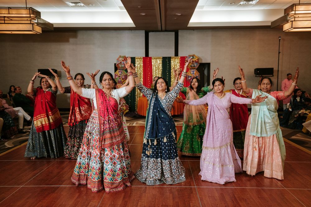 Group of dancers in colorful traditional Indian lehengas performing with raised arms on stage.