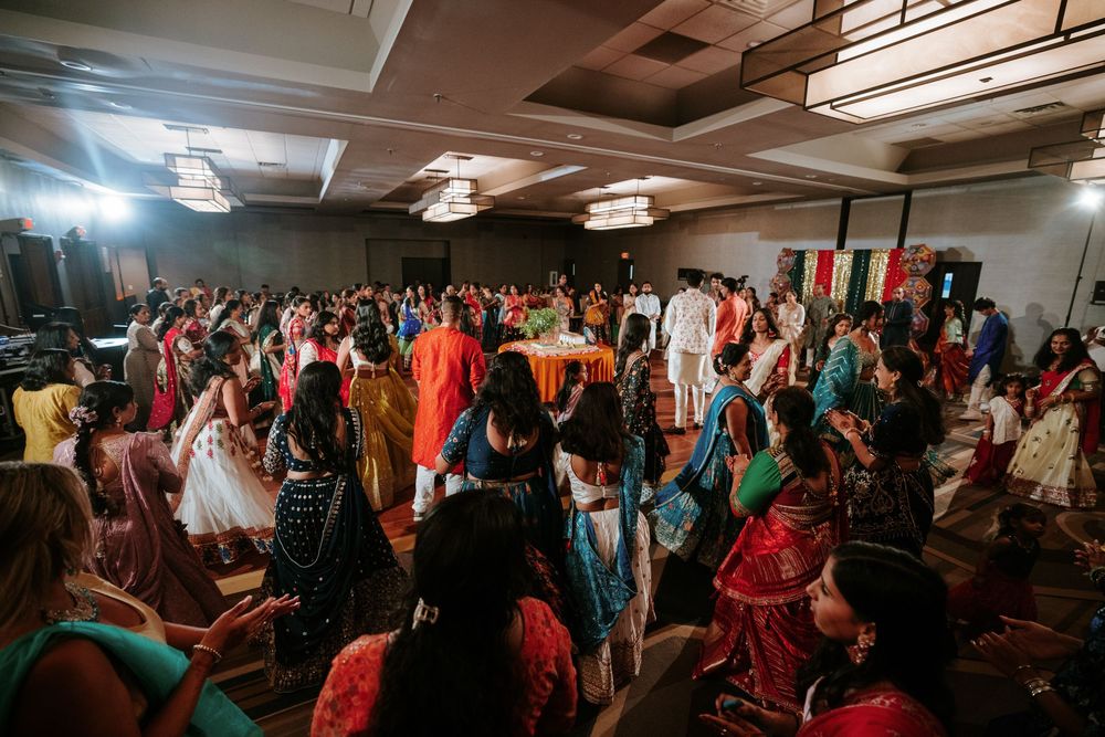 Large group of wedding guests dancing and celebrating in a decorated indoor venue.