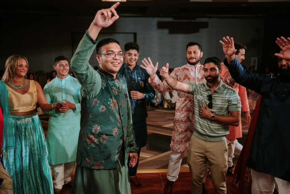 People dancing and celebrating at an indoor reception with colorful lighting and festive atmosphere.