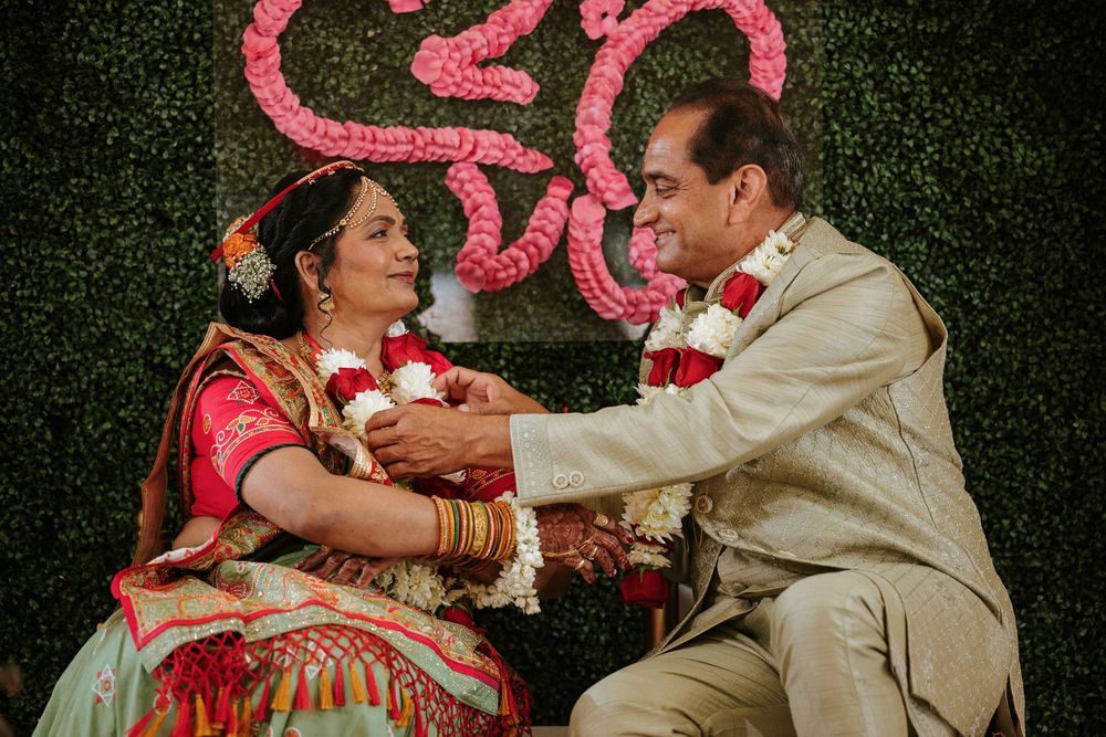 Traditional Indian wedding couple performs a cultural ceremony ritual in front of a green hedge backdrop.