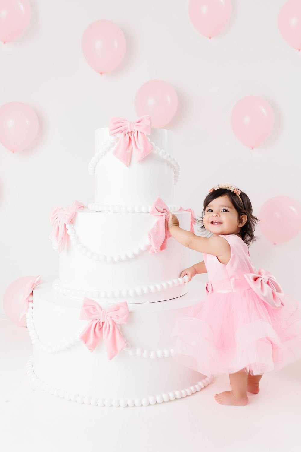 A child in a pink tutu dress poses gracefully against a white backdrop with pink balloon decorations.