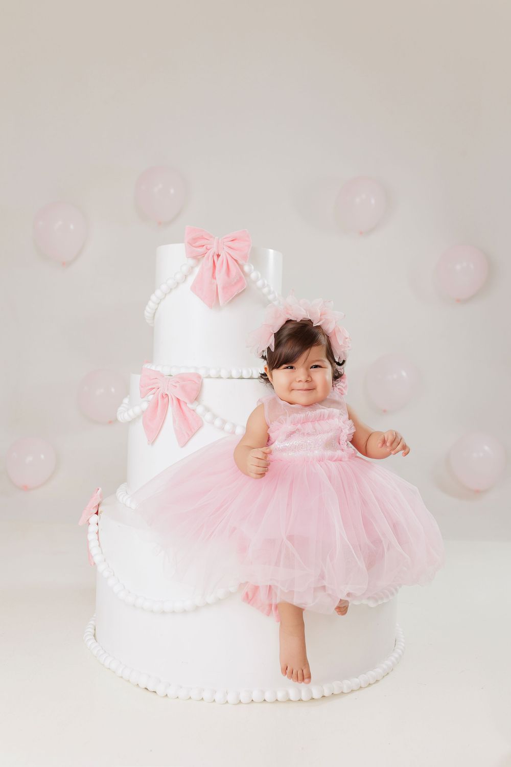Sweet pink and white cake smash photography session with tulle dress and delicate bow details against light backdrop.