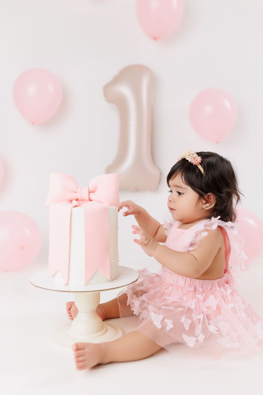 Pink first birthday cake smash photo setup with balloons and tulle dress on white background.