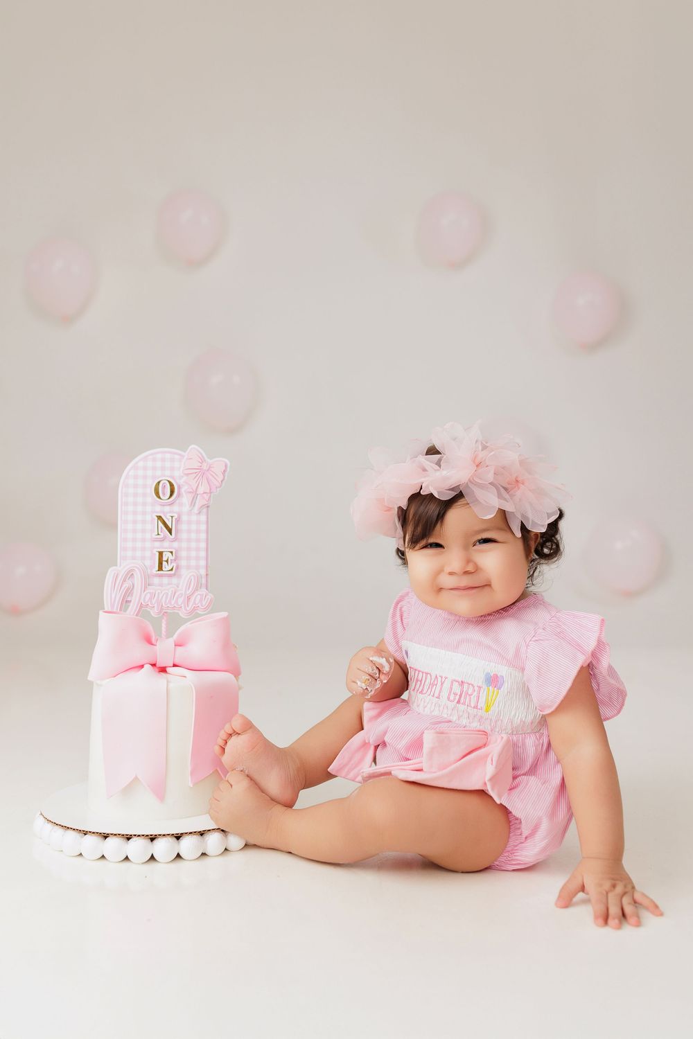 Pink themed first birthday photo shoot setup with decorative blocks and soft pastel bubbles in the background.