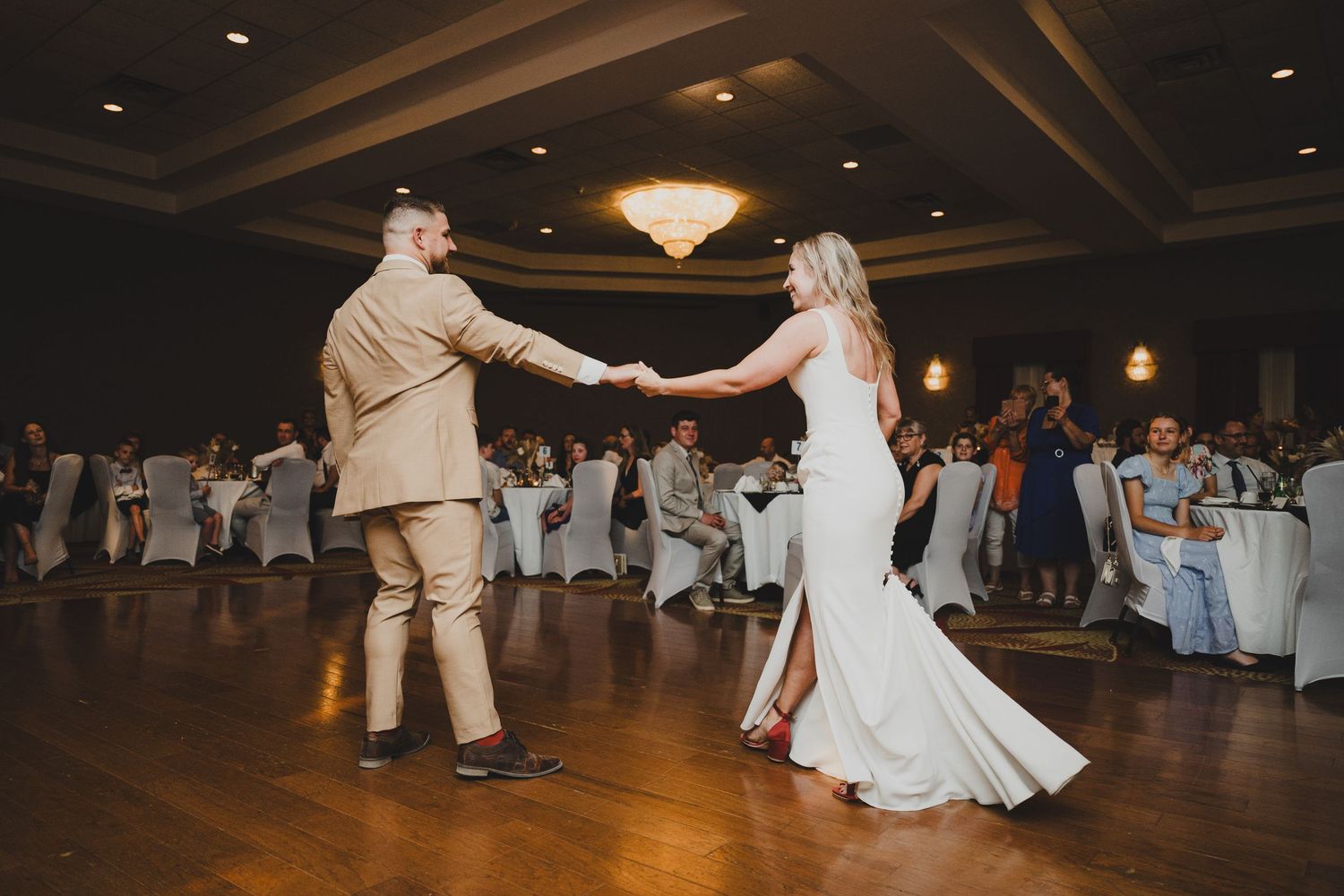 Dancers perform a lively swing dance routine on a wooden dance floor at an elegant ballroom reception.