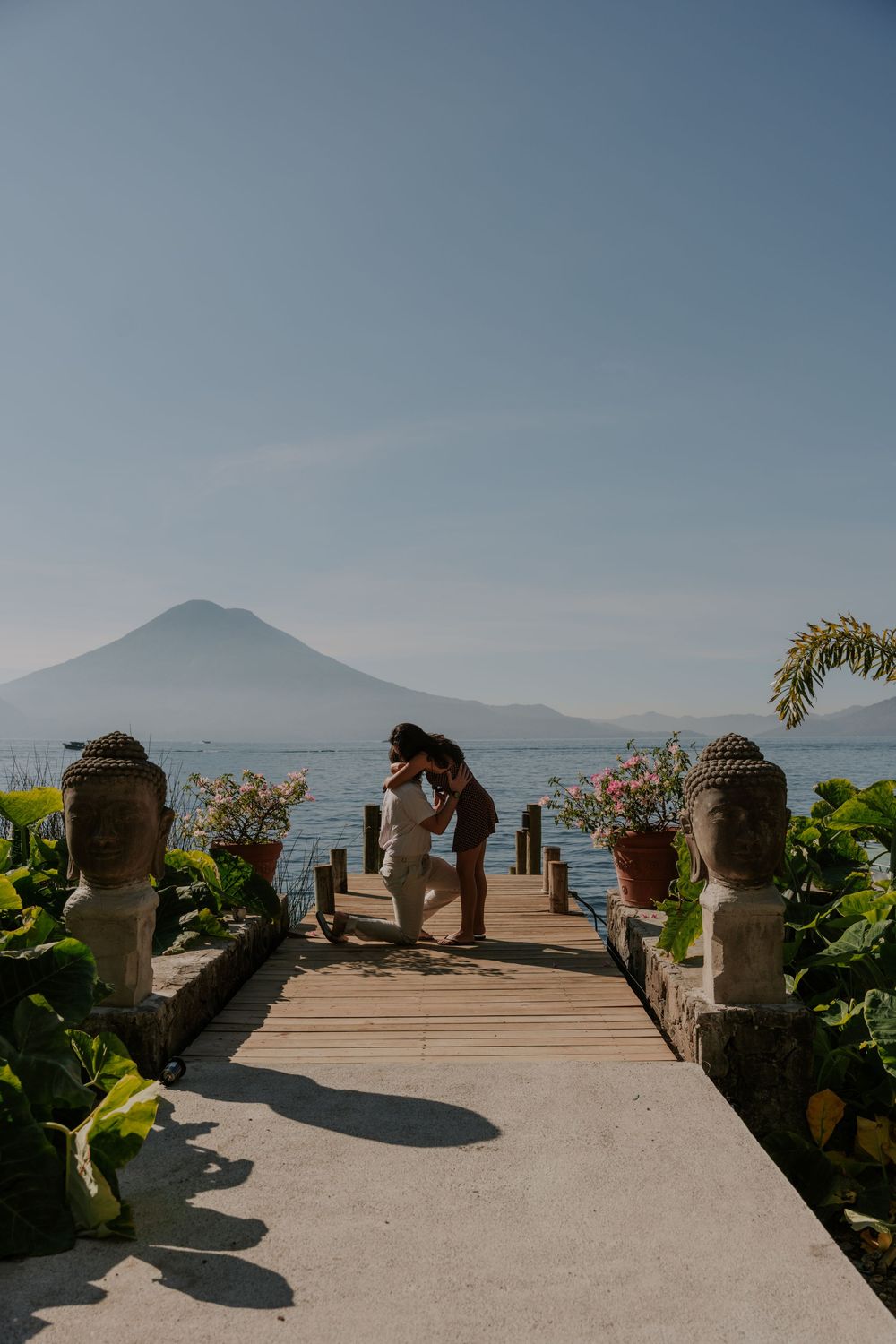 A scenic waterfront walkway with stone pillars overlooking Lake Atitlan and volcanoes in Guatemala on a sunny day.