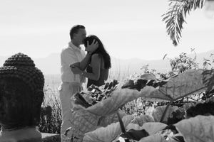A black and white photograph showing a romantic moment with a Buddha statue in the foreground.