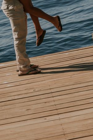 Feet walking on a wooden dock by calm blue water on a sunny day.