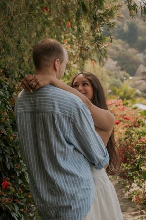 Couple embracing in a lush garden with colorful flowers and green foliage surrounding them.