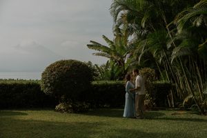 A tropical beachfront wedding ceremony setup with white chairs and palm trees overlooking the ocean at sunset.
