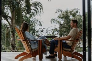 People relaxing in wooden Adirondack chairs on a patio overlooking a scenic mountain landscape.