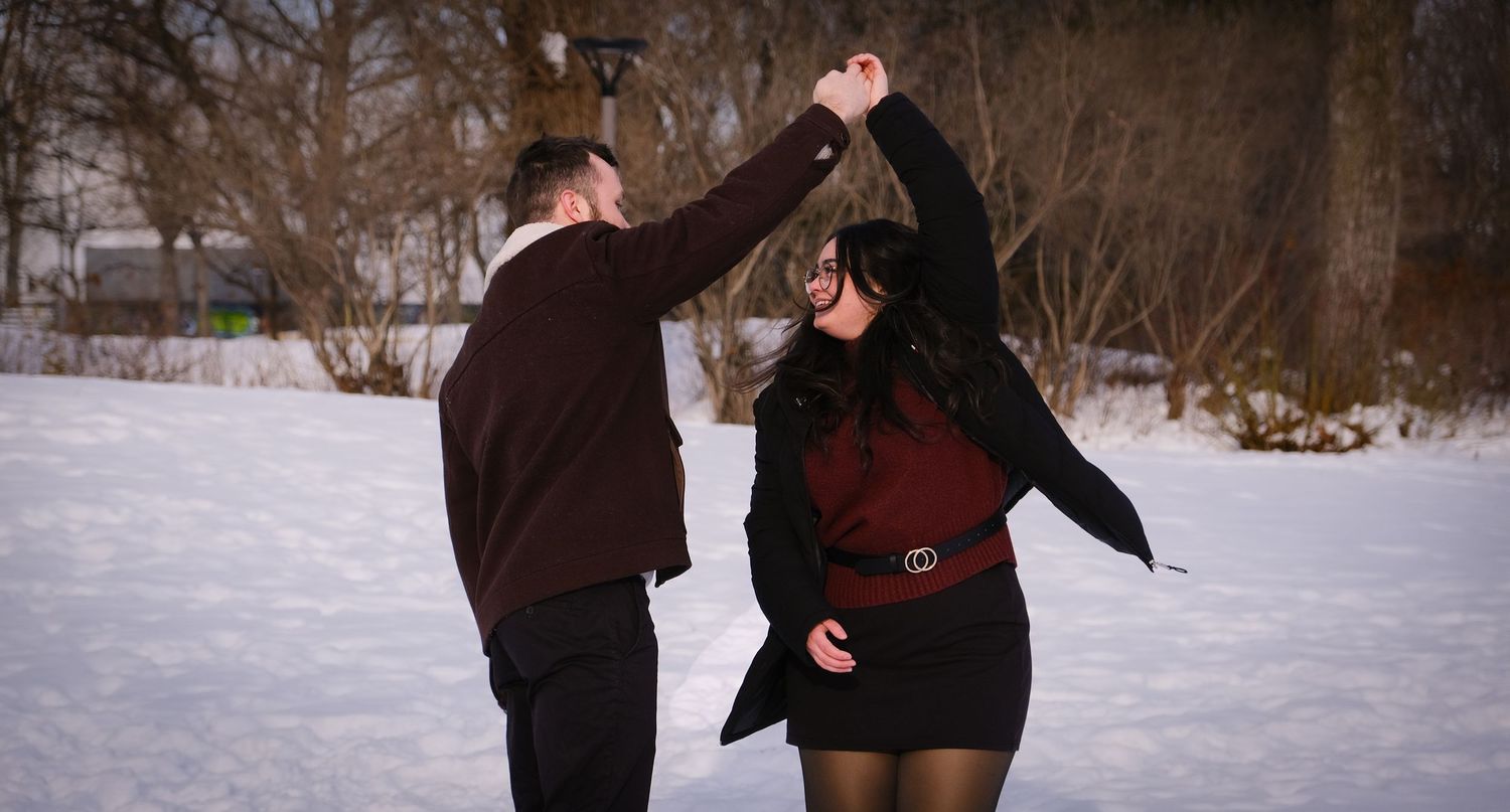 Couple dancing together in a snowy winter landscape with playful movements.