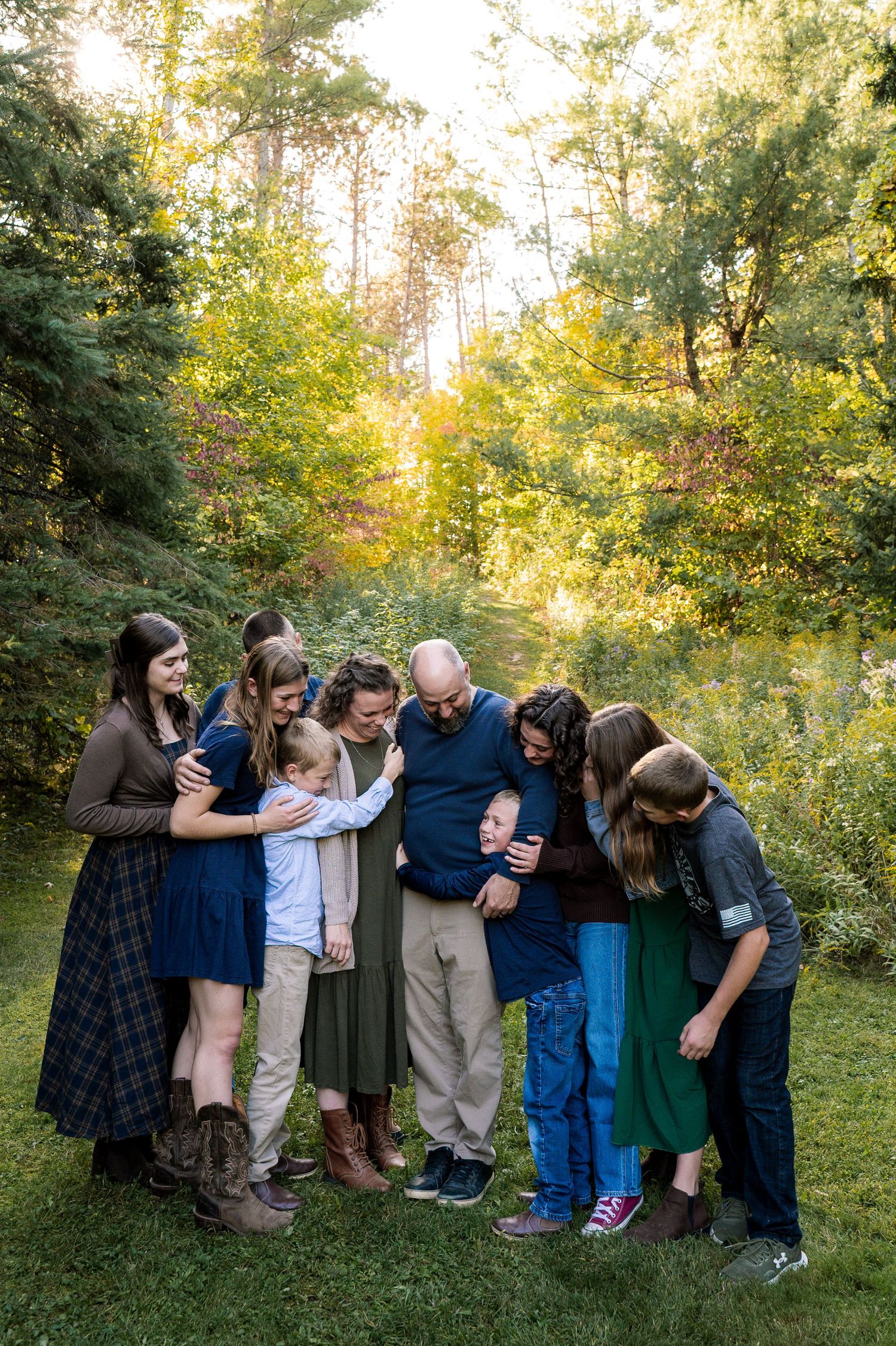 A group of people stand together outdoors in a wooded area during golden hour lighting.