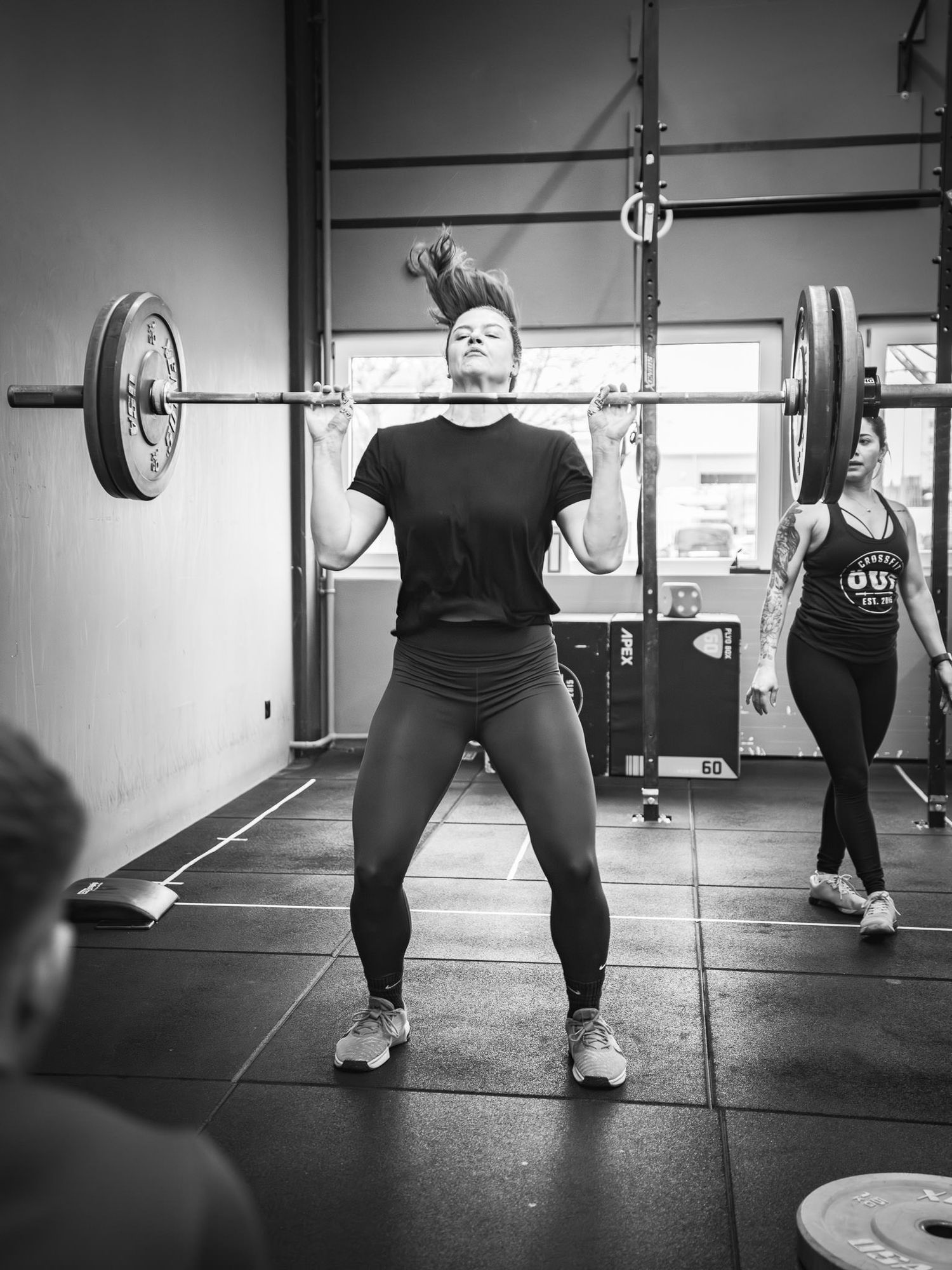 Low angle view of people performing barbell exercises on a gym floor.