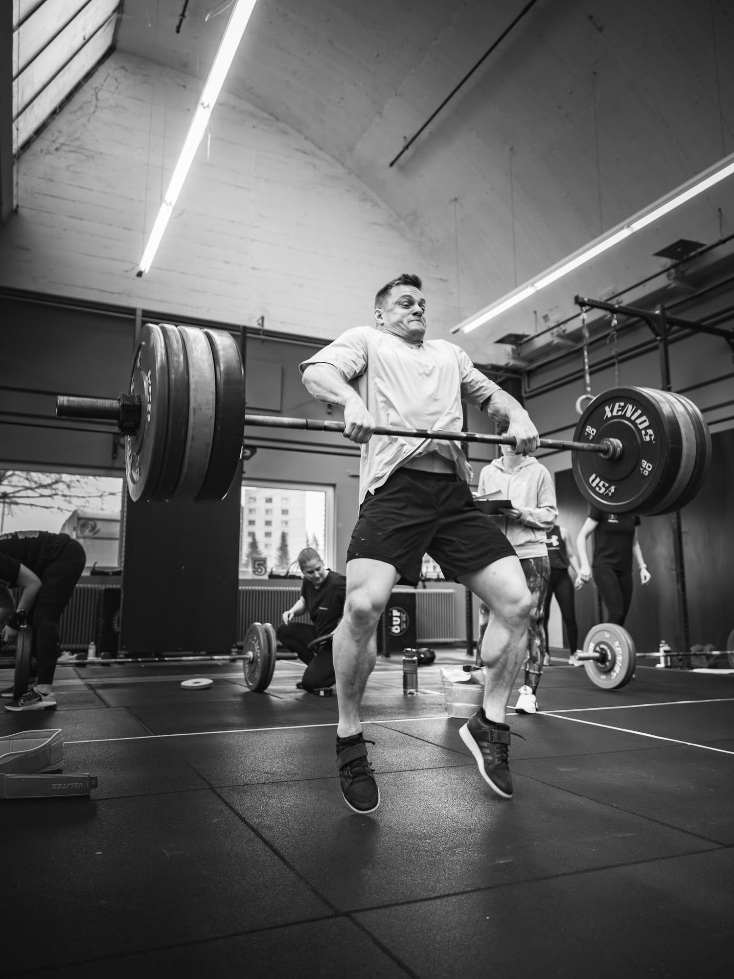 Wide angle shot of weightlifters performing synchronized barbell exercises in a gym.