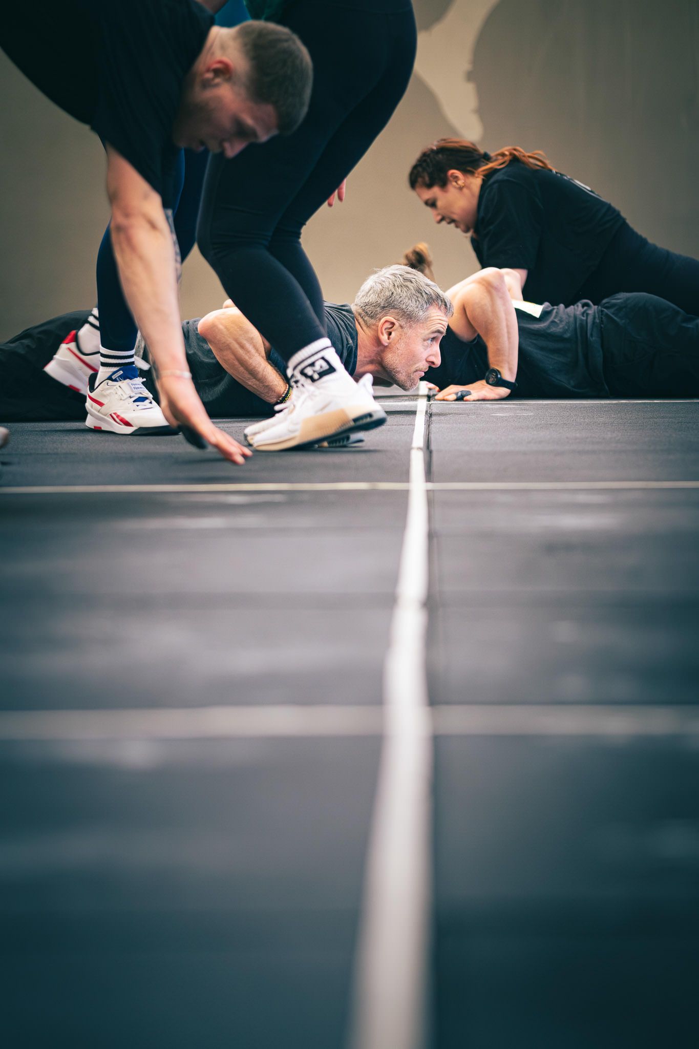 Side view of athletes in plank position on a gym floor during workout.