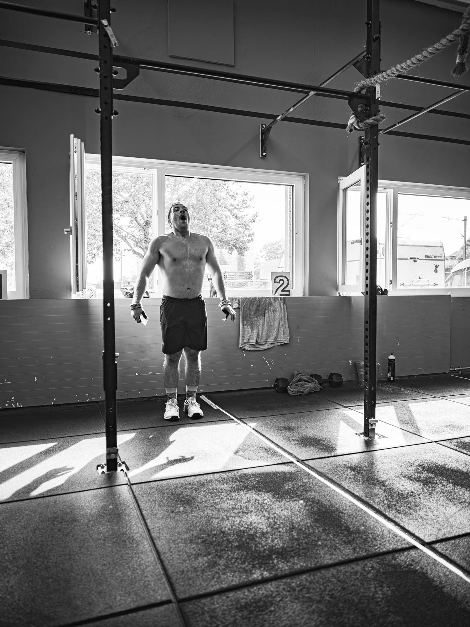 Silhouetted figures in sunlit gym with exercise equipment and windows.