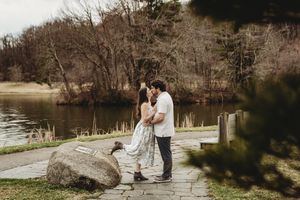 Couple embracing romantically by a serene pond in a lush park setting during early spring.