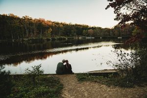 Couple sitting together by a tranquil lake surrounded by autumn foliage at dusk.