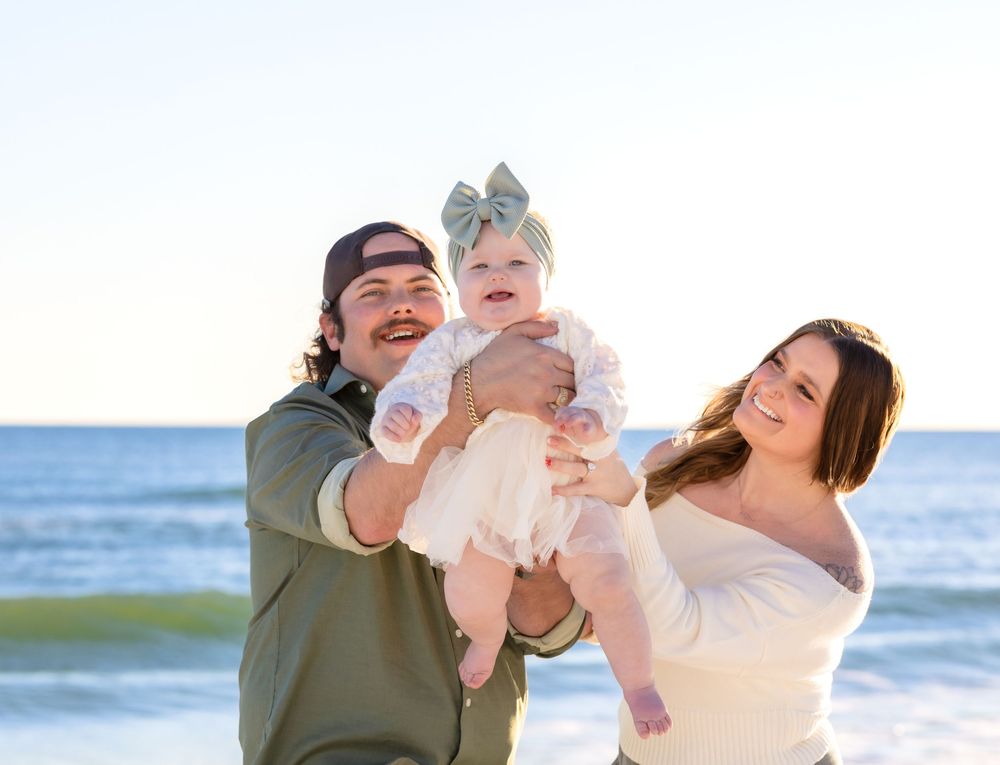 Happy family enjoying a playful moment together on a sunny beach with ocean waves in the background.
