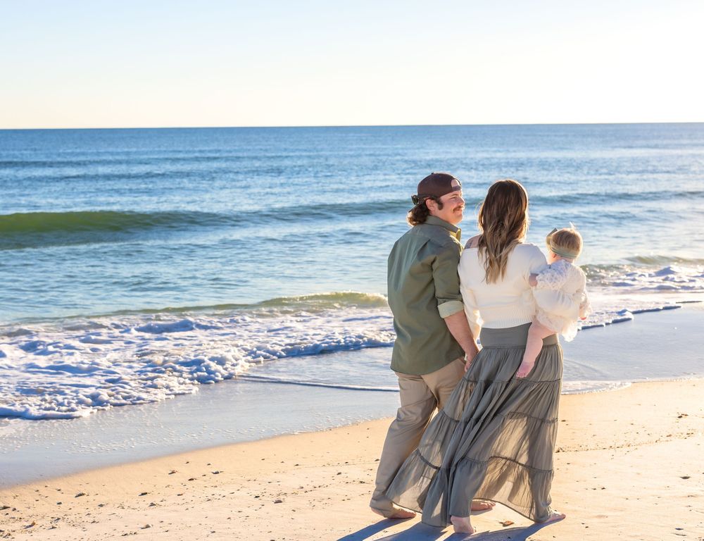 A family walks together along a peaceful sandy beach with gentle waves rolling onto the shore in the background.