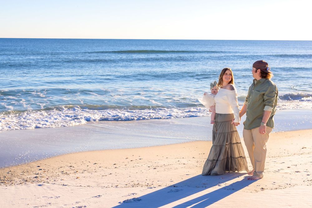 A couple walks along a sandy beach at sunset casting long shadows on the shore as waves roll in.