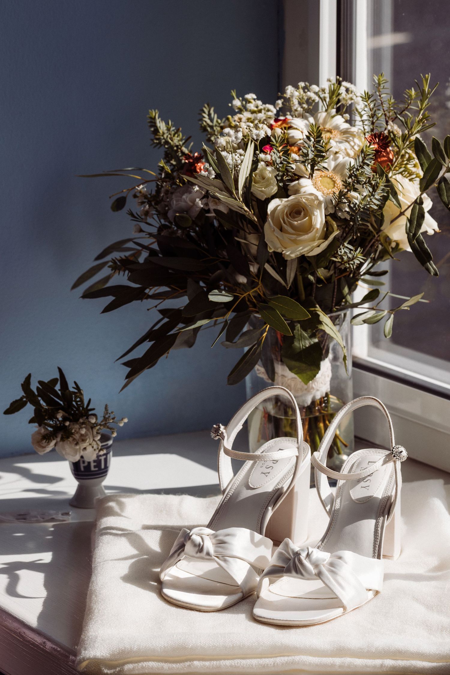 Elegant floral arrangement in white vase creates dramatic shadows on white surface in natural window light.