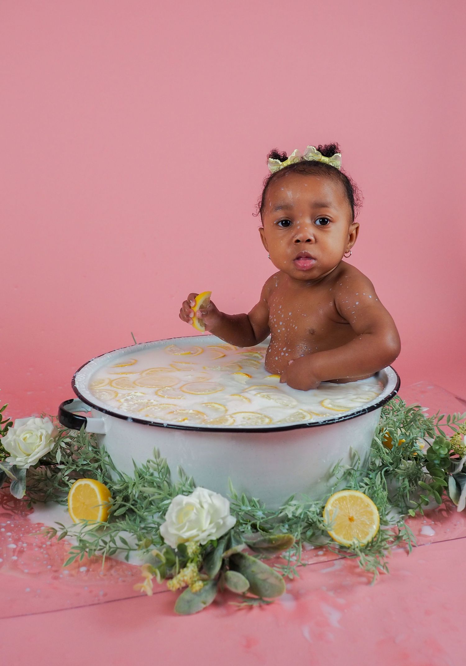 A milk bath photo setup with citrus and flowers on a pink background.