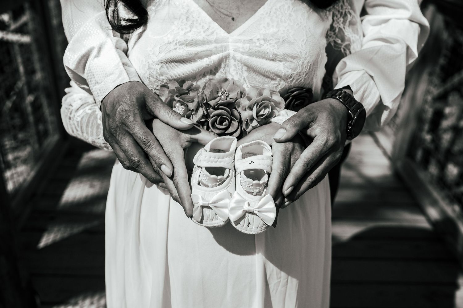 Close-up of hands holding tiny white baby shoes against a white dress.