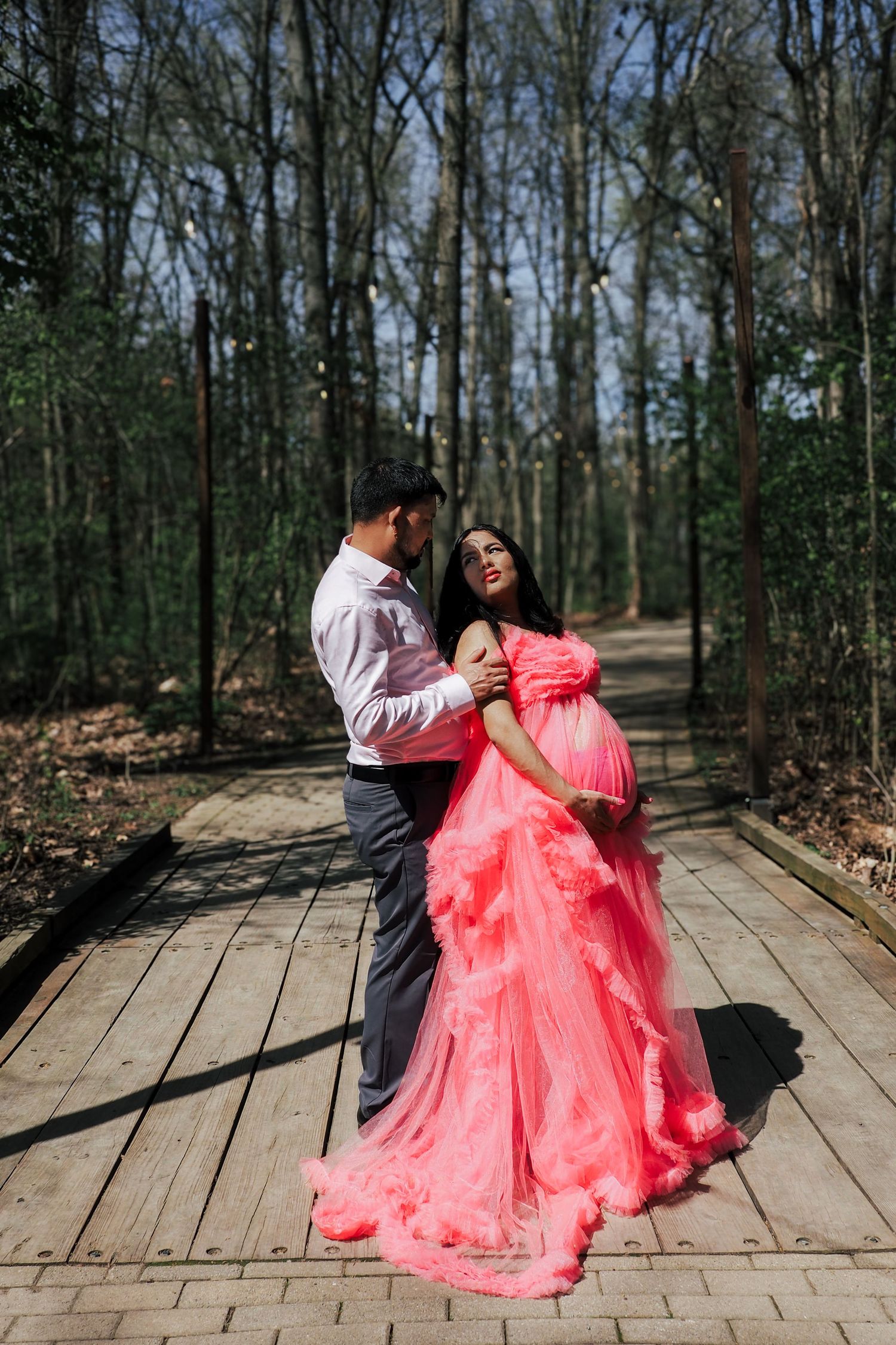 A couple sharing an intimate moment on a wooden path surrounded by trees.